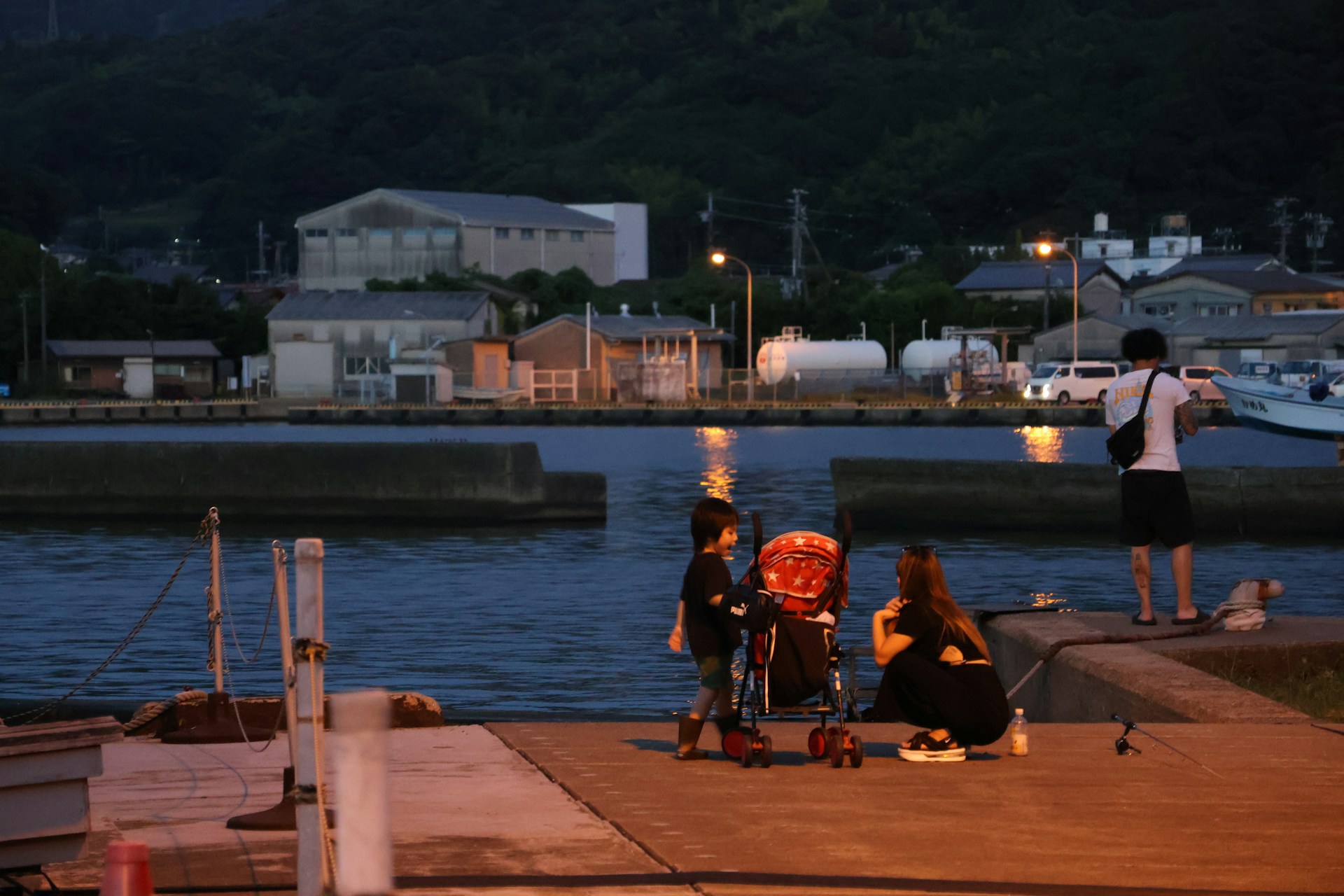 A mother and son fishing together at dusk by the water.