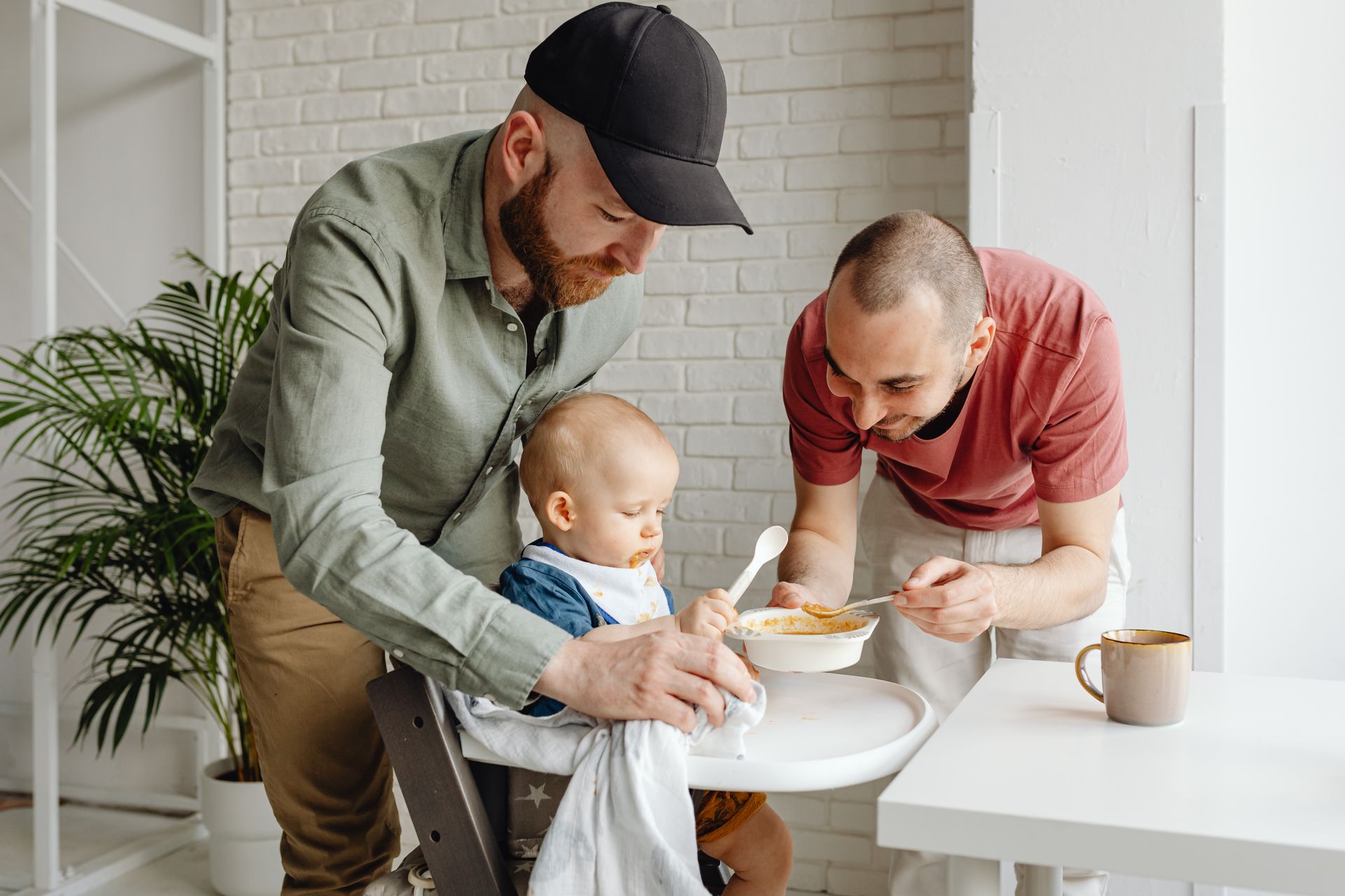 Two dads feeding their toddler at home.